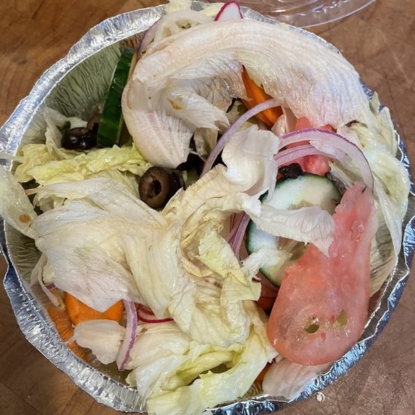 A fresh garden salad with lettuce, tomatoes, cucumbers, onions, carrots, and olives in a foil container.