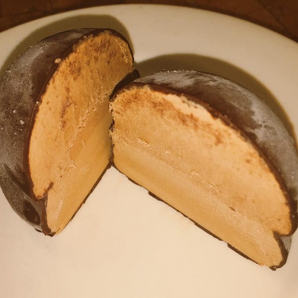 A chocolate-covered ice cream dessert, cut in half, revealing a light brown, creamy interior.