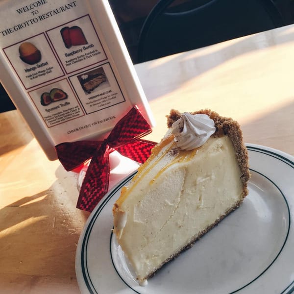 A slice of cheesecake with whipped cream and caramel drizzle on a plate next to a dessert menu.