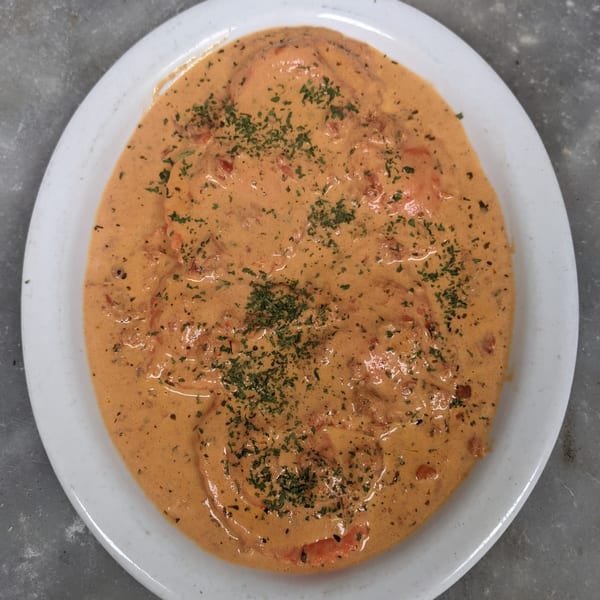 A white plate holds a creamy orange sauce with visible tomato pieces and green herbs.